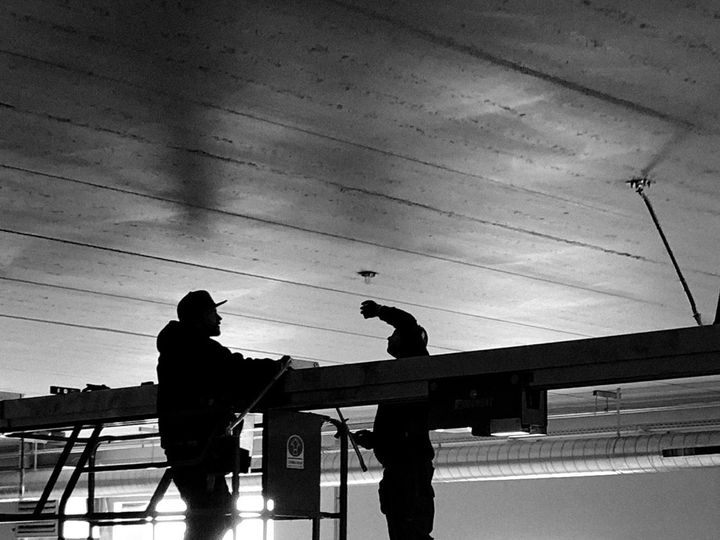 To montører i silhuet arbejder på en lift under et betonloft